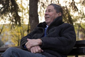 Obraz premium Portrait of happy senior man smiling, in the public park, outdoors. Old man relaxing outdoors and looking away. Portrait of elderly man enjoying retirement