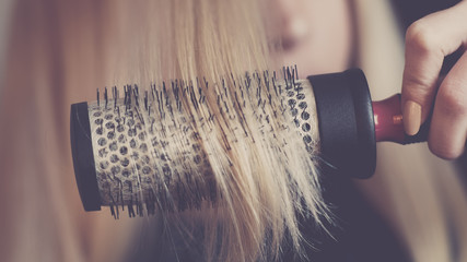 Round brushing combs long blond hair closeup.