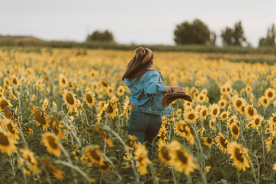 Young woman with blue denim jacket and hat running in a field of sunflowers
