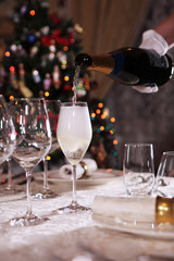 Champagne pours into a tall glass goblet. Macro photo without a face in the interior. Christmas tree out of focus.