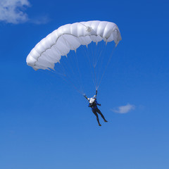 Skydiver with a whitel parachute on a blue sky background.