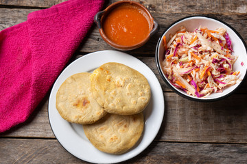 Salvadoran pupusas with coleslaw and tomato sauce on wooden background