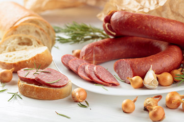 On a white wooden table sausage with bread, rosemary, onion and pepper.