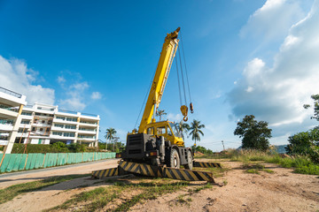 Yellow automobile crane with risen telescopic boom outdoors. Mobile construction crane on a constructin site. Crane machine stand by waiting for work under the construction building. Heavy industry.