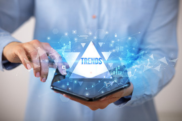 Businessman holding a foldable smartphone with TRENDS inscription, business concept