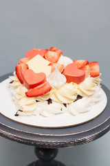 Heart shaped pavlova cake with fresh berries, strawberries, chocolate and meringues on grey background. 