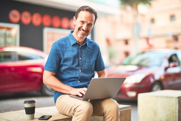 Middle age handsome businessman using laptop drinking take away coffee smiling on the street