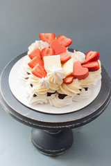 Heart shaped pavlova cake with fresh berries, strawberries, chocolate and meringues on grey background. 