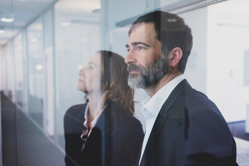 Portrait of businesswoman and businessman in office looking through glass pane