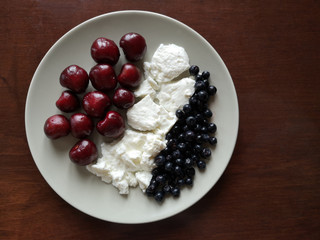 Sweet cherries and blueberries with cottage cheese or yoghurt on white plate. Top view photo of natural and healthy food. Summer breakfast with fresh organic dairy and berry ingredients.