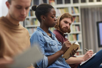 Serious African woman sitting and making notes in her notepad together with her colleagues during a lecture