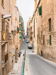 Fototapeta na wymiar Traditional Maltese street in Valetta, Malta with traditional balconies and slope. Travel and tourism in Malta concept. Cityscape of Valletta. Architecture of Valetta.