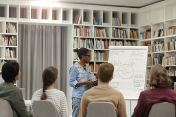 African young woman pointing at whiteboard and holding the presentation for young people in the library