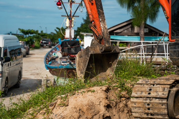 Small orange excavator on a ground against blue sky and sea for a works on construction site. Small tracked excavator standing on a ground with a blue sea on background. Heavy industry.