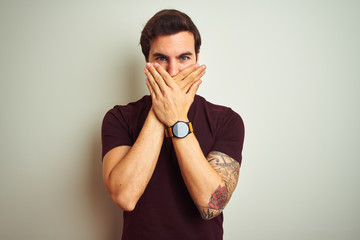 Young handsome man with tattoo wearing purple casual t-shirt over isolated white background shocked covering mouth with hands for mistake. Secret concept.