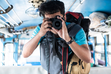 Young Thai male traveller taking a photo with dslr camera on bus while travelling.