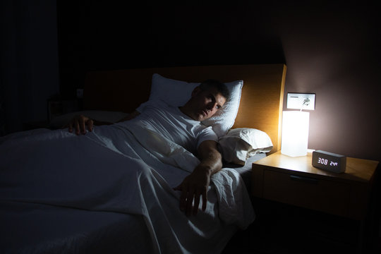 A Man With Insomnia Looks At The Clock At Dawn From The Bed With Concern