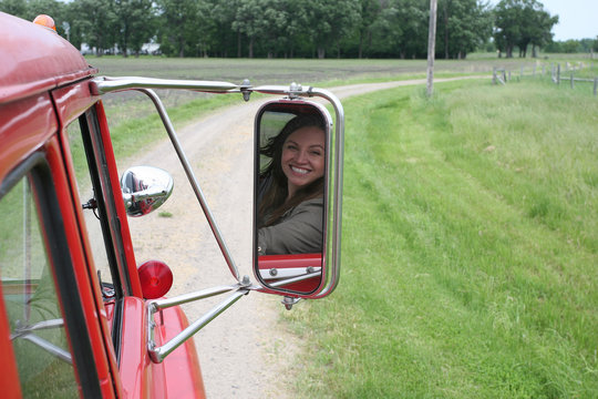 A young woman looking back and smiling in a truck mirror.