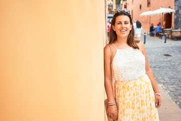 Fototapeta premium Beautiful girl leaning on orange wall, young friendly woman smiling happy on a sunny day of summer