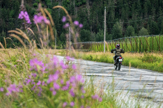 A woman rides her motorcycle on a cloudy summer day.