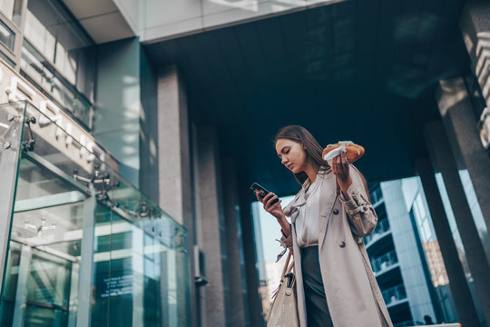 A girl with a pie in her hand looks anxiously at the phone on a city street