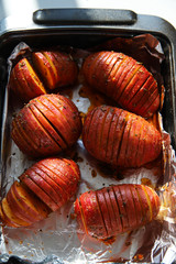 Oven baked potato hassleback with olive oil, spices and herbs in foil. Healthy dinner concept. Roasted vegetables on marble background with sunlight and strong shadows