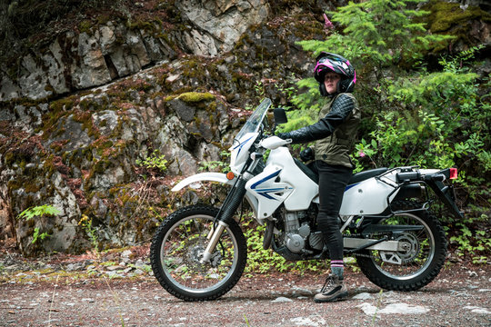 A women riding a motorcycling stops on a gravel road.