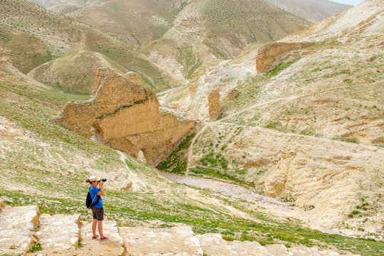 Hiker taking photos in front of Ruins of ancient aqueduct in Wadi Quelt, Jericho