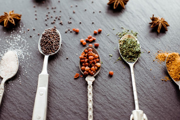 A selection of cooking spices on vintage spoons on a slate board