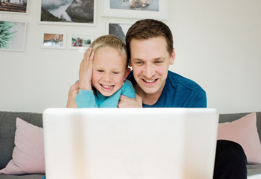 father and son laughing at home whilst looking at a laptop at home