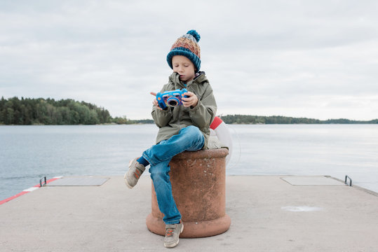 young boy sitting by the beach looking at his pictures on his camera
