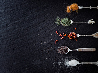 A selection of spices on vintage spoons on a slate chopping board