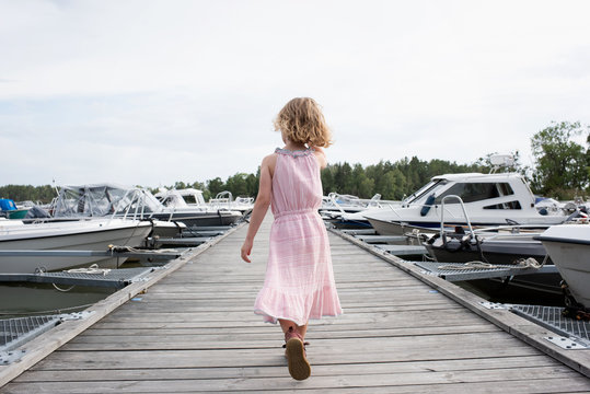 young blonde girl walking on a pier looking at the boats at sea