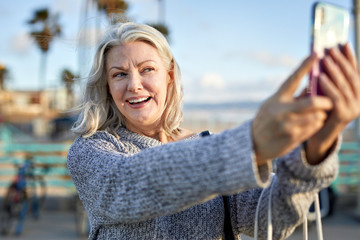 Smiling senior woman taking selfie with smart phone at beach during sunset