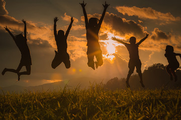 The silhouette of the team of children jumping playing with joy in the mountains in the setting sun