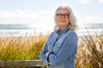 Smiling thoughtful woman with arms crossed standing at Manhattan Beach during sunny day
