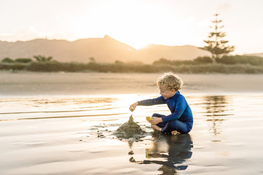 Young child building sandcastle at beach in New Zealand at dusk