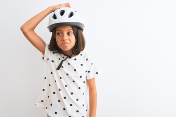 Beautiful child girl wearing security bike helmet standing over isolated white background confuse and wonder about question. Uncertain with doubt, thinking with hand on head. Pensive concept.