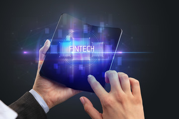 Businessman holding a foldable smartphone with FINTECH inscription, new technology concept