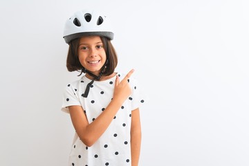 Beautiful child girl wearing security bike helmet standing over isolated white background cheerful with a smile of face pointing with hand and finger up to the side with happy and natural expression