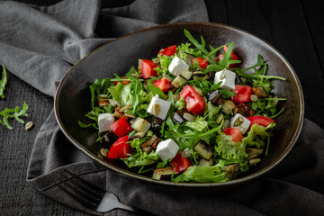 Vegetarian nutritious salad of arugula, baked eggplant and zucchini, pumpkin seeds, cherry tomatoes, feta cheese. Restaurant menu. Background black boards.