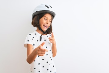 Beautiful child girl wearing security bike helmet standing over isolated white background pointing...
