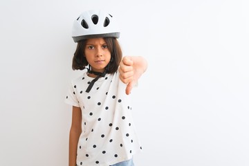 Beautiful child girl wearing security bike helmet standing over isolated white background looking unhappy and angry showing rejection and negative with thumbs down gesture. Bad expression.