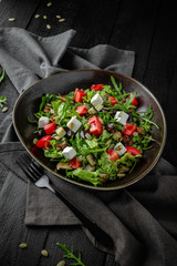 Vegetarian nutritious salad of arugula, baked eggplant and zucchini, pumpkin seeds, cherry tomatoes, feta cheese. Restaurant menu. Background black boards.