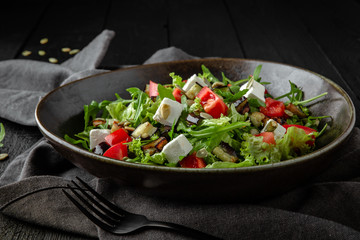 Vegetarian nutritious salad of arugula, baked eggplant and zucchini, pumpkin seeds, cherry tomatoes, feta cheese. Restaurant menu. Background black boards.