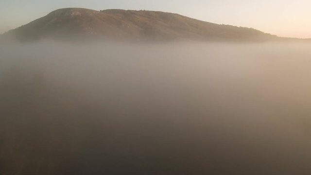 The remain of the reef of the ancient sea, composed of limestone - shikhan Kushtau. Fog on the Belaya river. Aerial view.