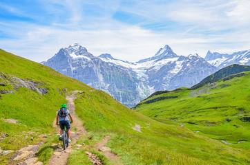 Fototapeta na wymiar Mountain biker riding downhill the beautiful summer Alpine landscape. Snowcapped mountains in the background. Photographed on the trail from Grindelwald to Bachalpsee. Active vacation