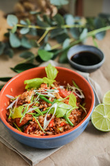 Bowl of stir fried udon noodles garnished with black sesame seeds and fresh mint with green chopsticks