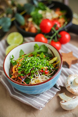 Bowl of stir fried udon noodles garnished with black sesame seeds and fresh mint with green chopsticks