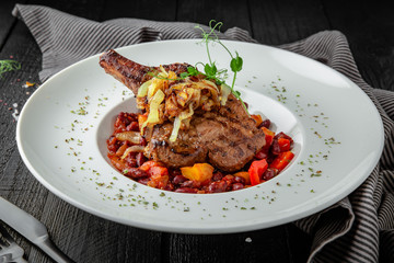 Bone steak in vegetable stew. Beef or pork shoulder, rib. Restaurant menu. Background black boards.